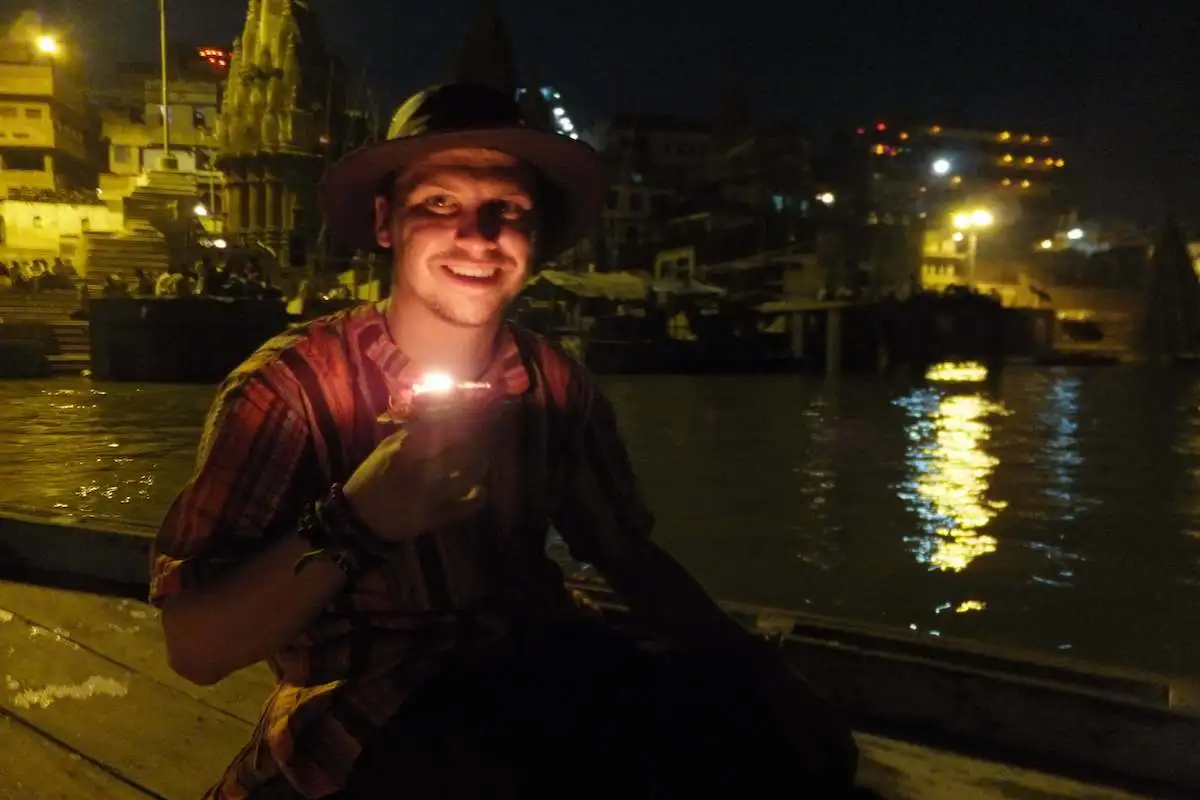 Un homme assis sur un bateau la nuit à Varanasi en Inde tenant une offrande de bougies