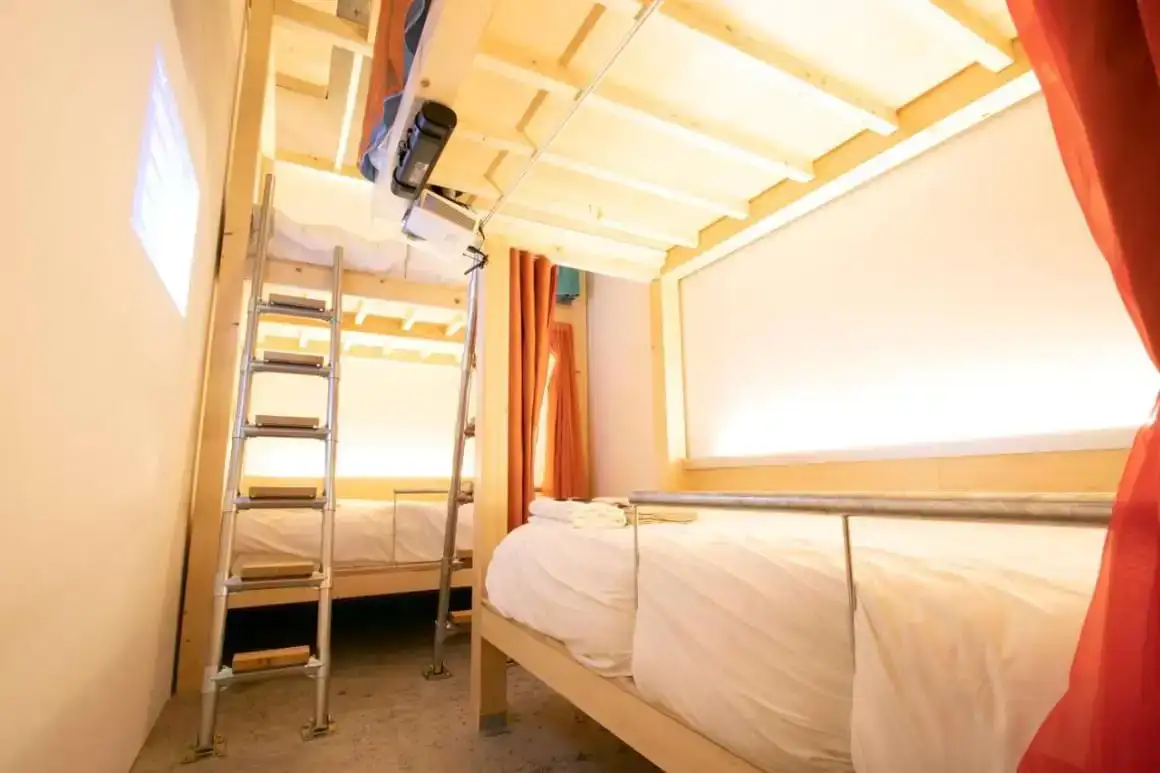 Kamar asrama dengan pencahayaan hangat di Theatel Sapporo, dihiasi dengan tempat tidur susun dan tangga