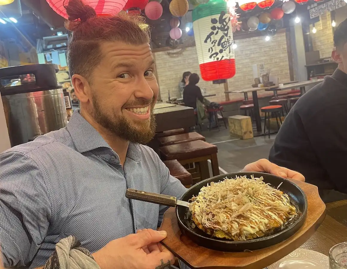 Manger de l'okonomiyaki à Osaka au Japon lors d'une tournée gastronomique de rue.