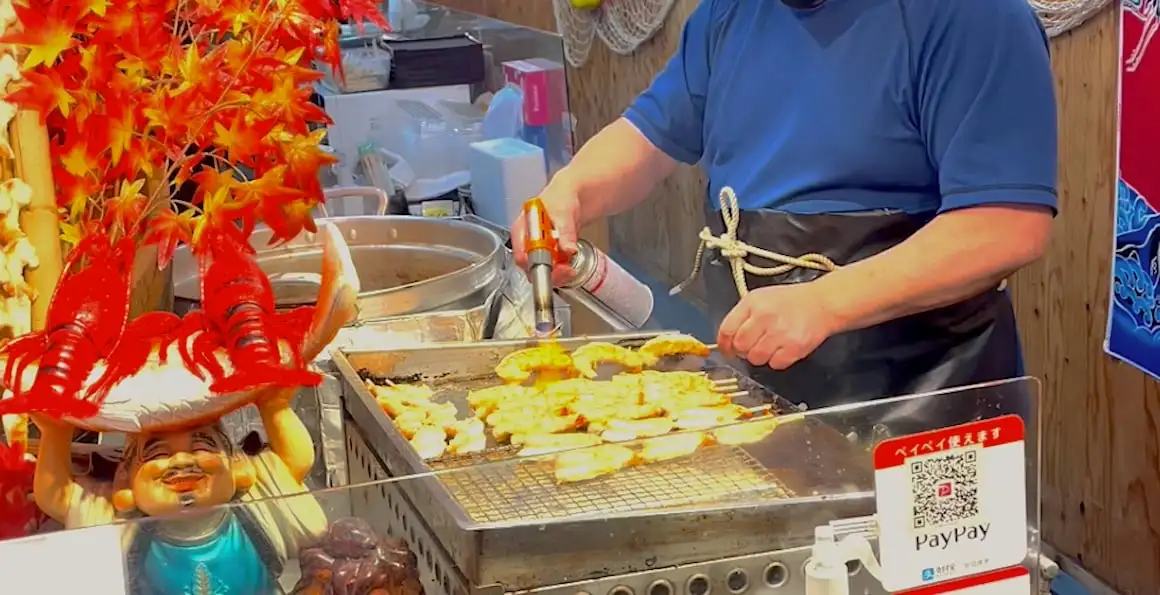 Un homme cuisine des crevettes dans un stand de nourriture de rue sur le marché de Kyoto, au Japon.