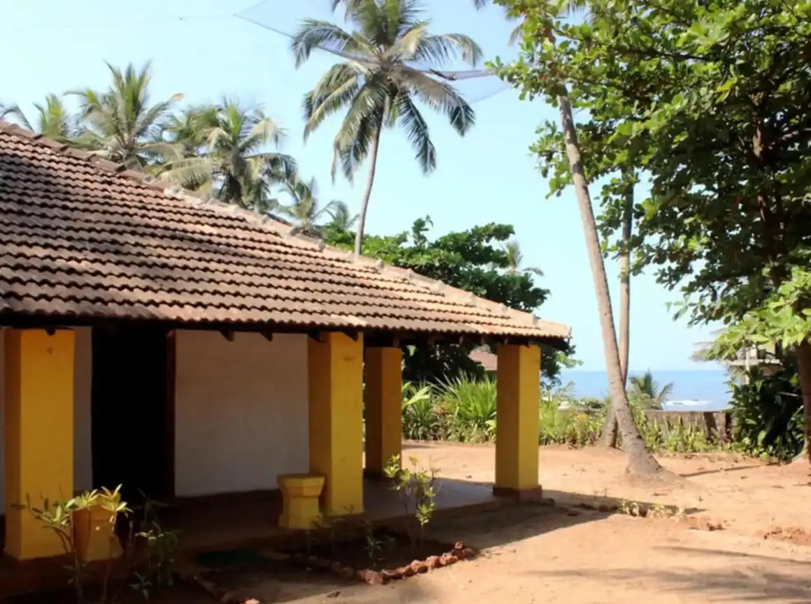Goan Beach House jaune simple avec un toit de chaume entouré de palmiers