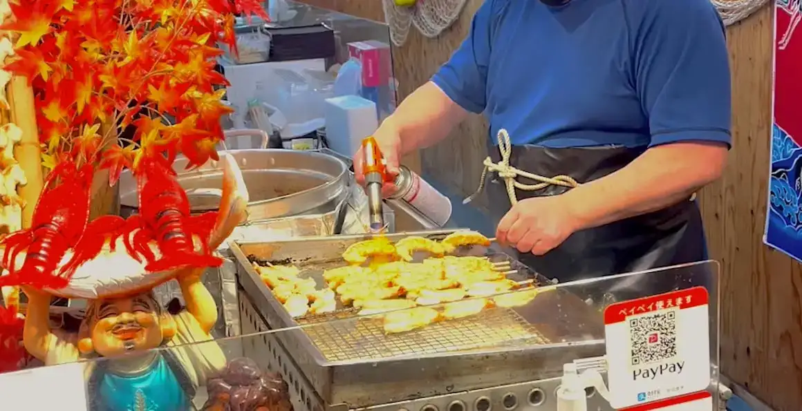 Seorang pria memasak udang di kedai jajanan kaki lima di pasar di Kyoto, Jepang.