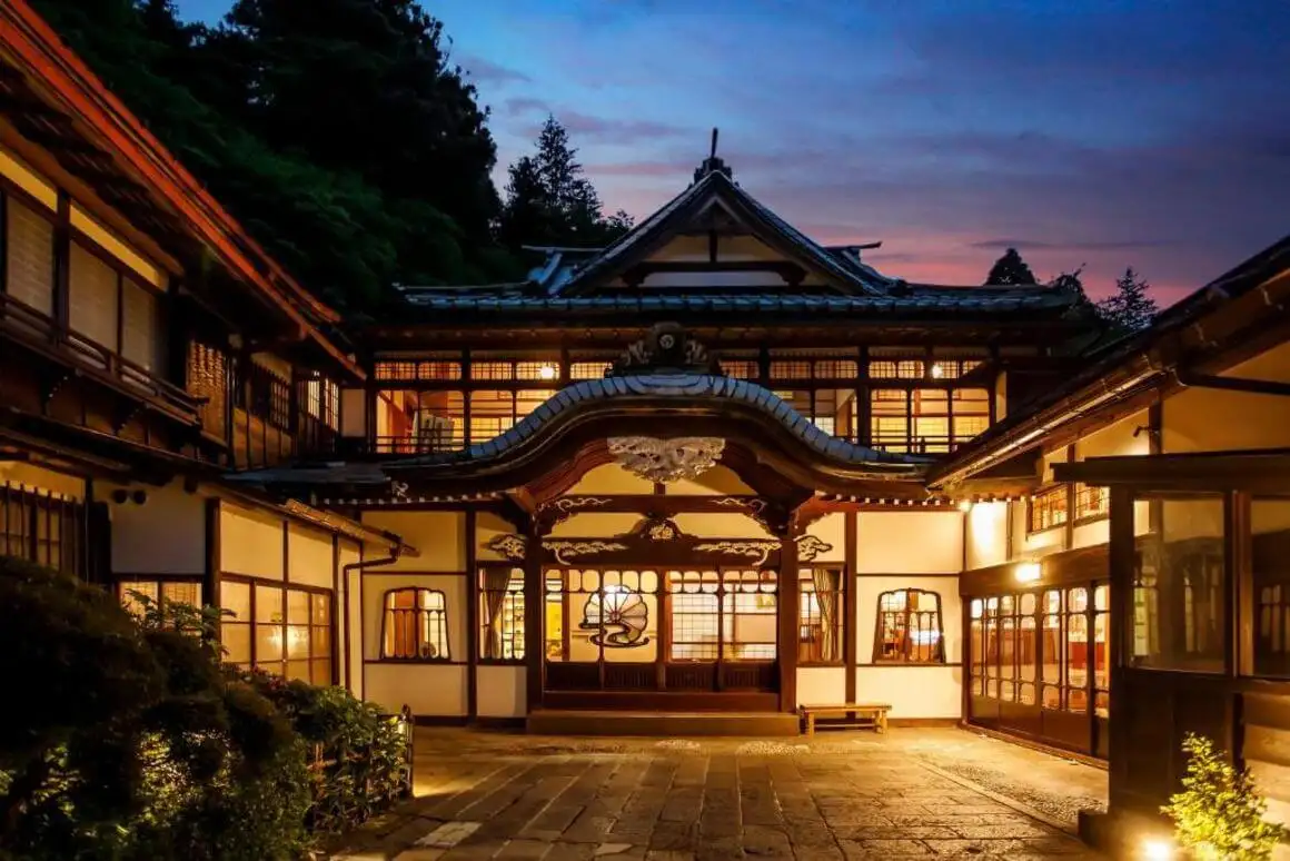箱根の旅館の広々としたベッドルームには、白い布団 2 枚、シーティングエリア、バルコニーが備わっています。