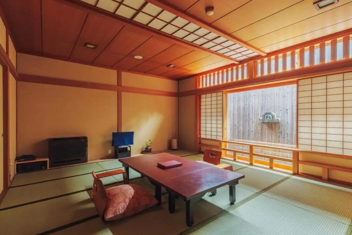 利春旅館の一室で、真ん中にテーブルと椅子があり、障子があり、庭園の景色を眺めることができます。