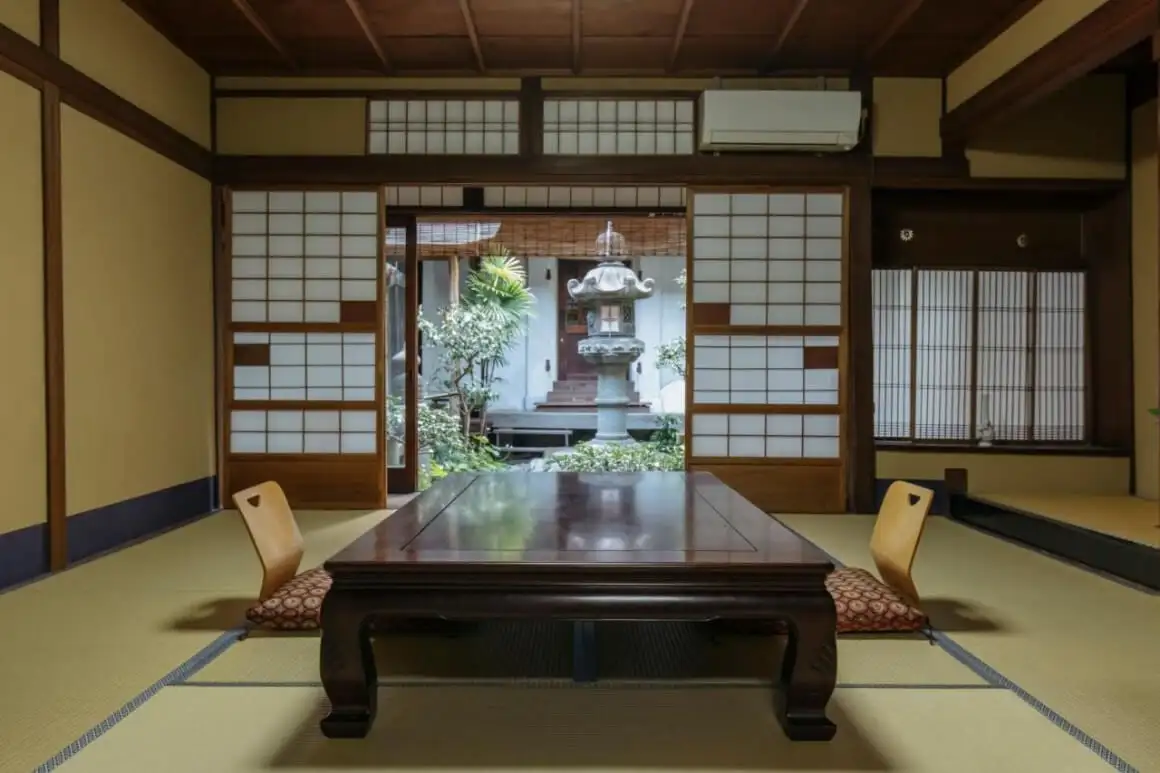 築100年の町家ゲストハウスの畳敷きのお部屋で、座卓と座布団が備わり、美しい庭園を望めます。