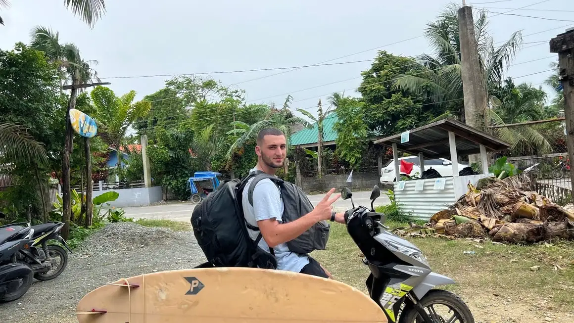 Joe på en skoter med surfbräda och Osprey Farpoint 40 - Endast handbagage