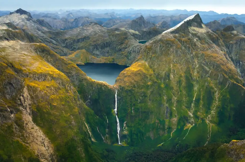une chute blanche dévalant une montagne de couleur verte en Nouvelle-Zélande sous un lac bleu circulaire