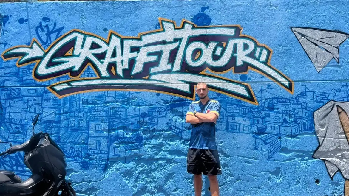 Joe estava em frente a um muro azul do Graffiti na Comuna 13, Medellín, Colômbia