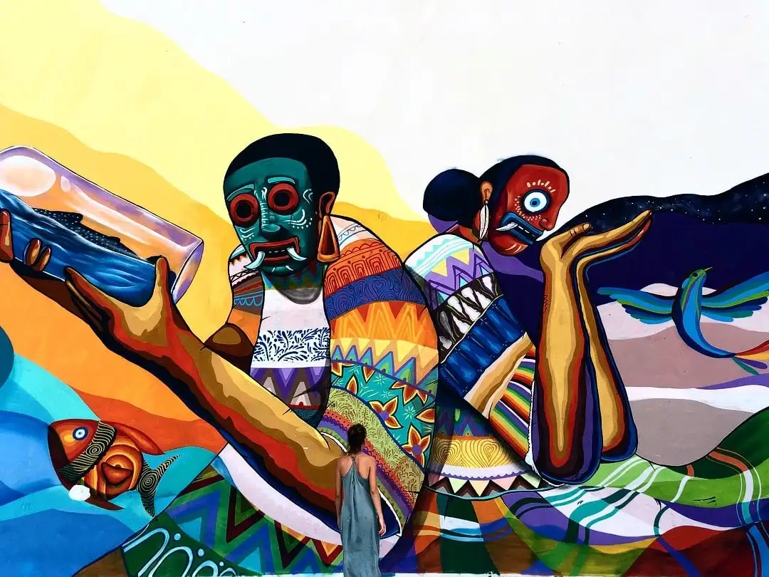 Um viajante LGBTQ fica em frente a um mural colorido no México