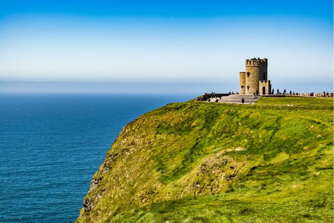 Um castelo à beira de uma colina verde tem vista para o oceano azul na Irlanda.