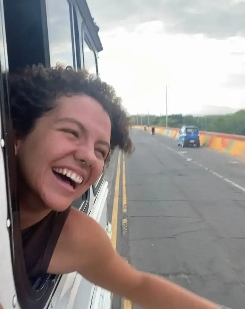 Une fille sourit en traînant à la fenêtre d'un bus au Salvador.