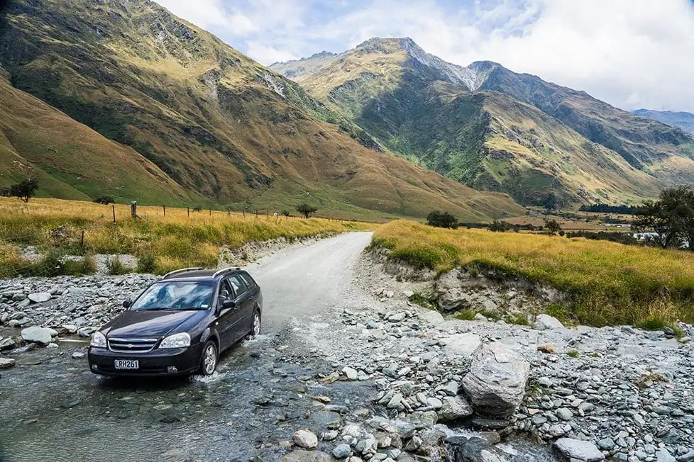 Une voiture traversant une rivière sur un chemin de terre avec des montagnes au loin près de Queenstown, Nouvelle-Zélande