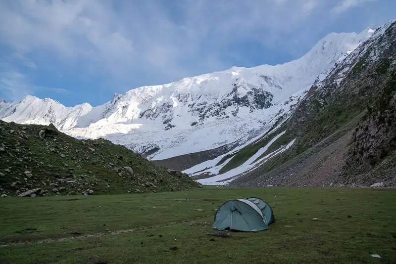 Tente verte dans un pré sous une randonnée en montagne massive au Pakistan