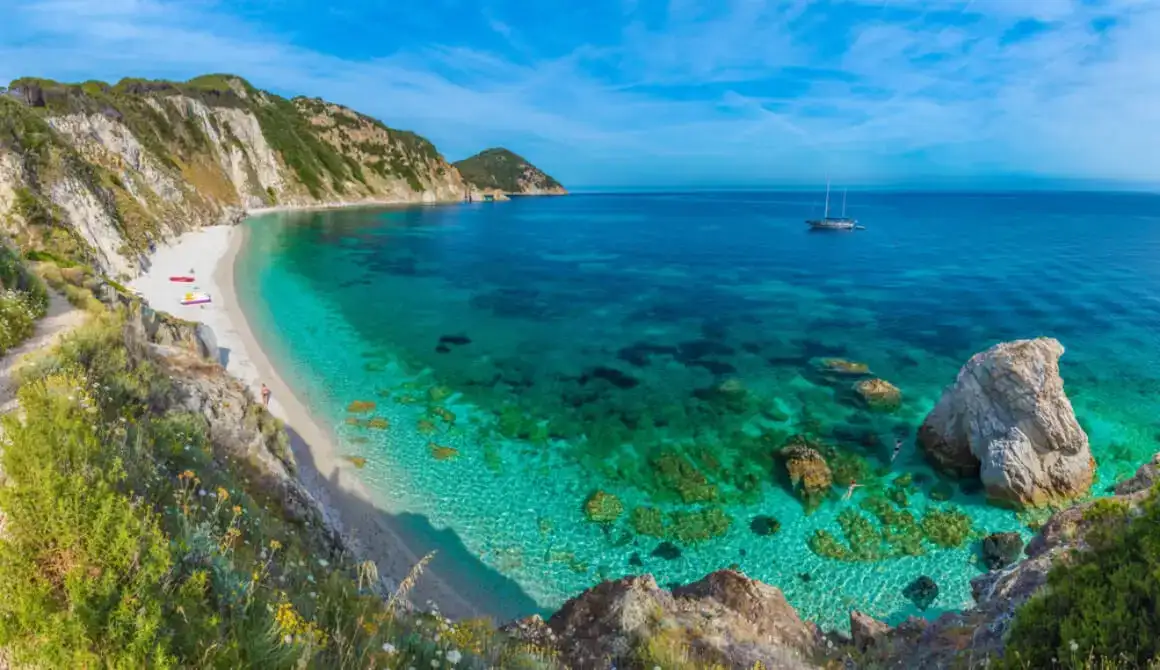 Плажа у Елби, Италија, окружена планинама са чамцем који плута у води