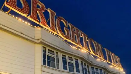 Um cara vestindo uma jaqueta verde clara e shorts em frente a uma casa azul de cabeça para baixo em um dia nublado em Brighton