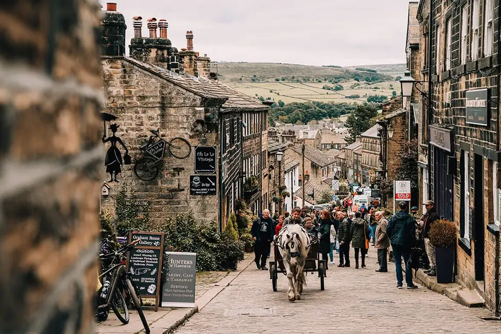 Um cavalo e um cartão em uma rua de paralelepípedos em uma vila em Yorkshire com os pântanos ao fundo