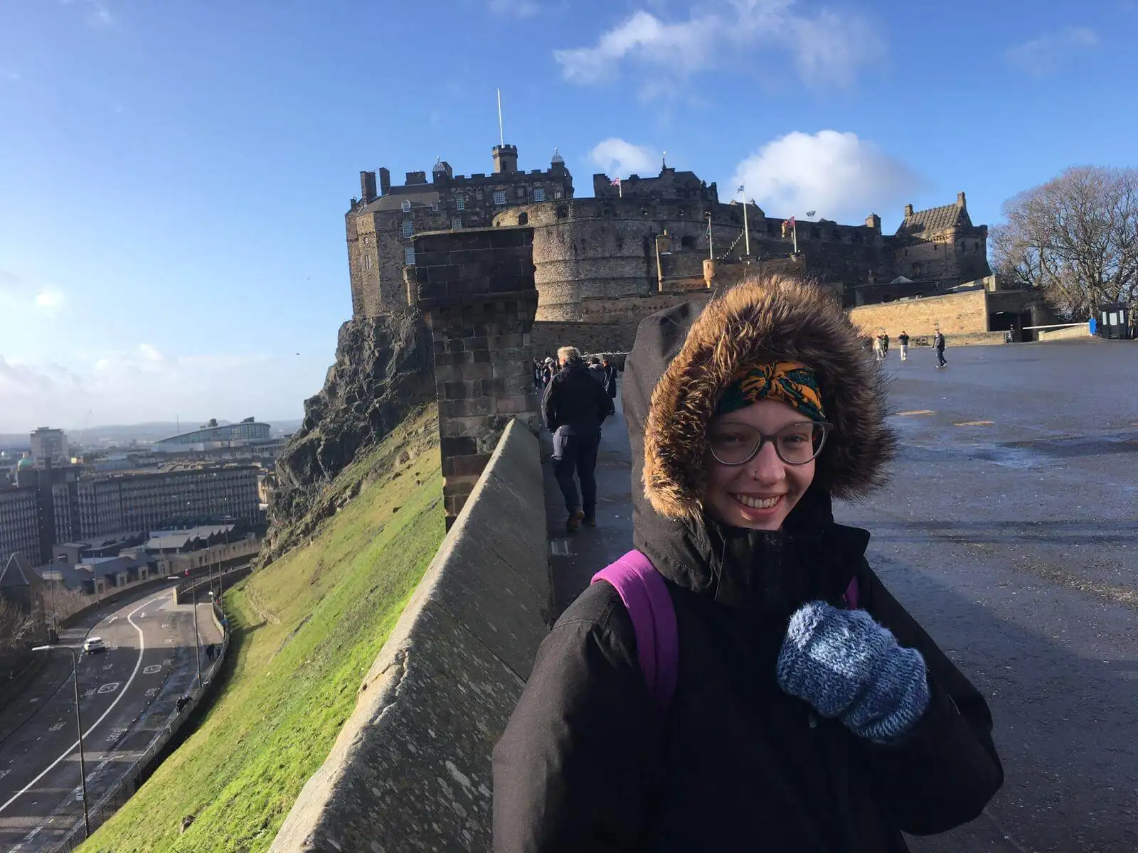 mulher vestindo um grande casaco de inverno e luvas grossas do lado de fora do Castelo de Edimburgo em um dia ensolarado