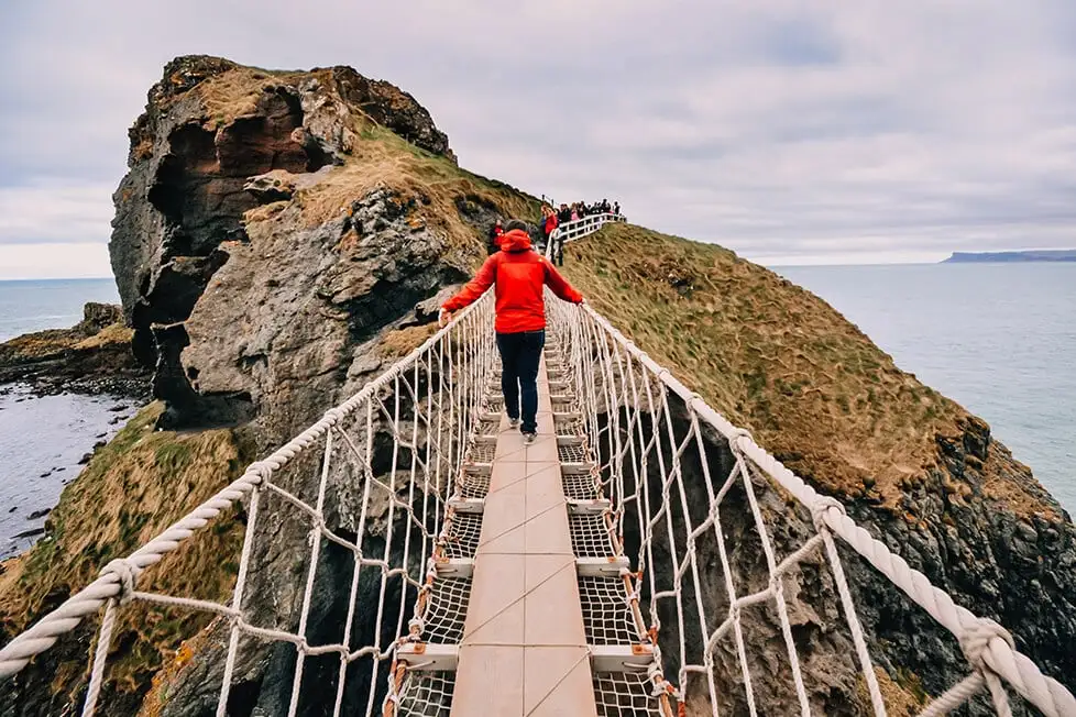 Uma pessoa atravessando a ponte de corda Carrick-a-rede, na Irlanda do Norte