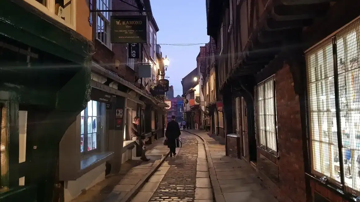 homem encapuzado caminha por uma antiga rua de paralelepípedos inglesa