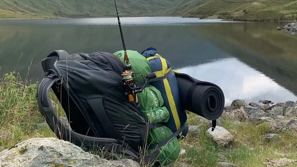 un sac à dos, une tente et une canne à pêche au bord d'un lac