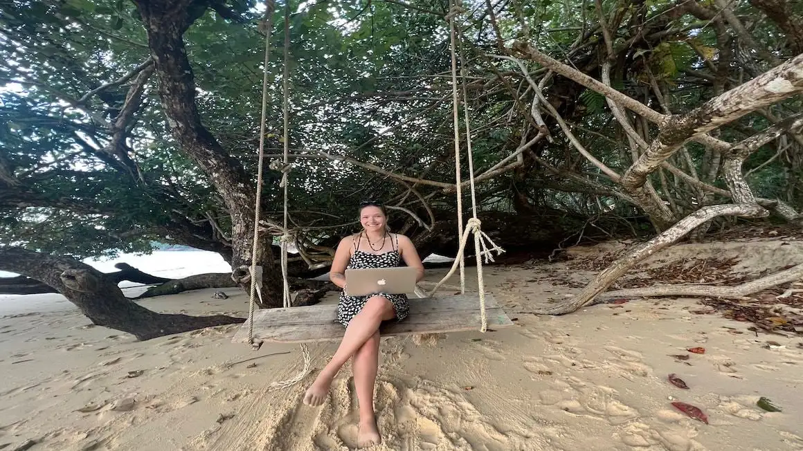 fille assise sur une balançoire sur une plage avec un ordinateur portable vivant la vie de nomade numérique