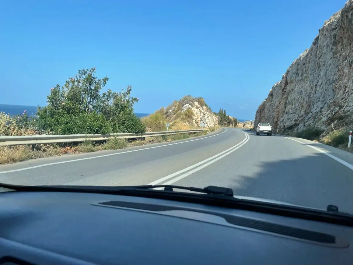 une fille debout au sommet d'une voiture blanche alors qu'elle regarde le coucher du soleil et l'océan