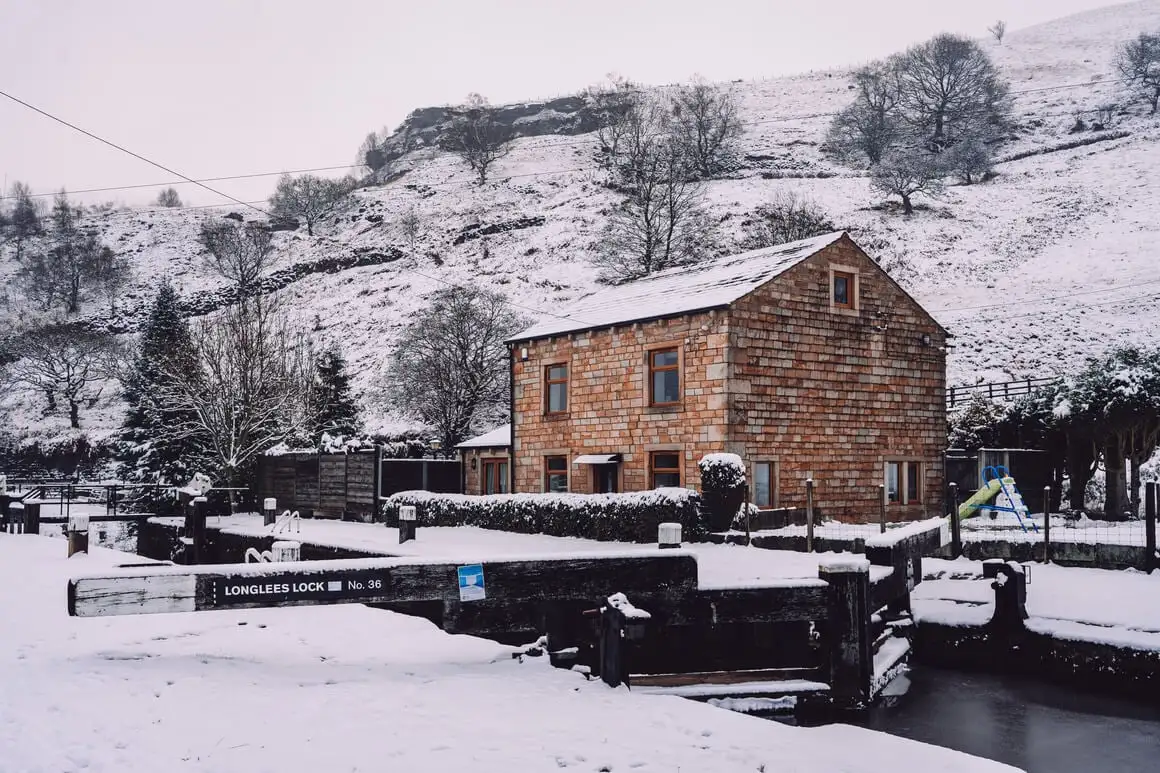Maison en brique devant un canal, collines couvertes de neige