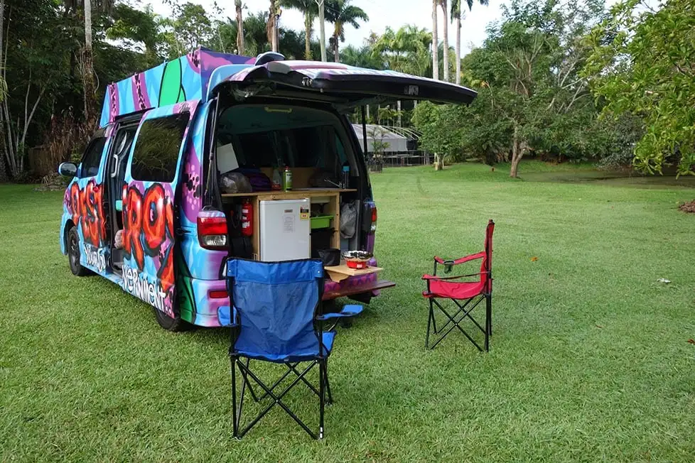 Un camping-car couvert de graffitis sympas dans un camping bordé de palmiers