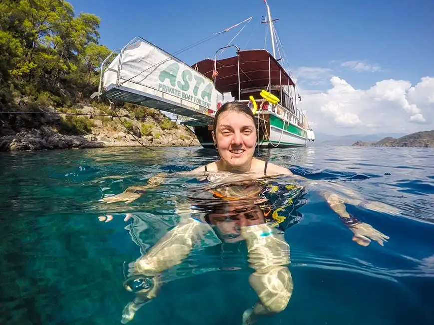 Nic nageant dans la mer au large des côtes turques dans une eau bleu clair avec un bateau derrière eux.