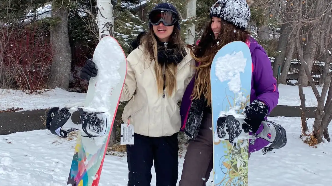 deux filles souriantes tenant des snowboards sur une montagne enneigée