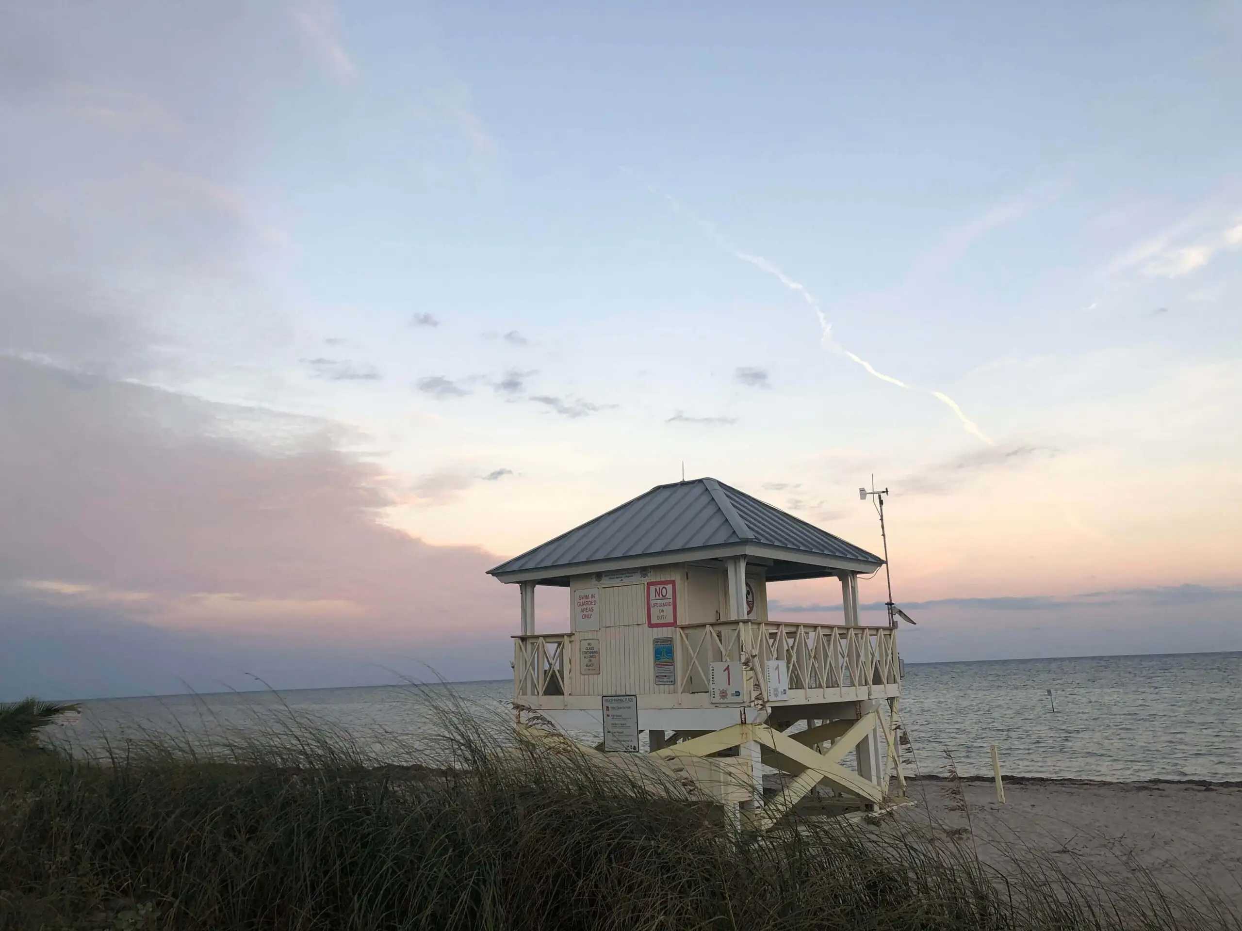 une cabane de sauveteur sur le sable derrière l'herbe de mer de la plage pendant un coucher de soleil pastel rose clair sur la plage de Key Biscayne à Miami en Floride