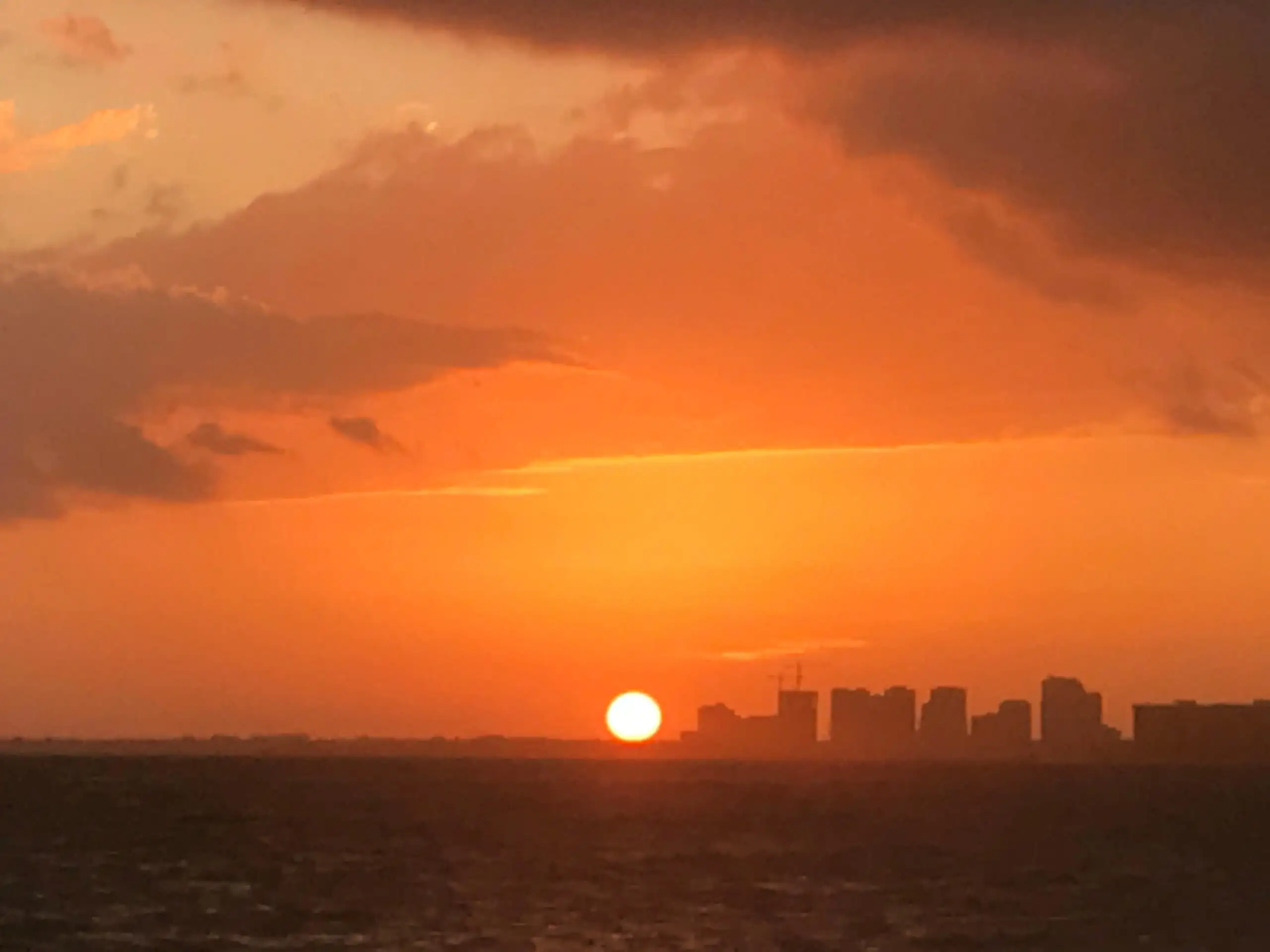 un coucher de soleil orange vif sur une plage avec quelques immeubles de grande hauteur en arrière-plan vu lors d'un séjour à Miami en Floride
