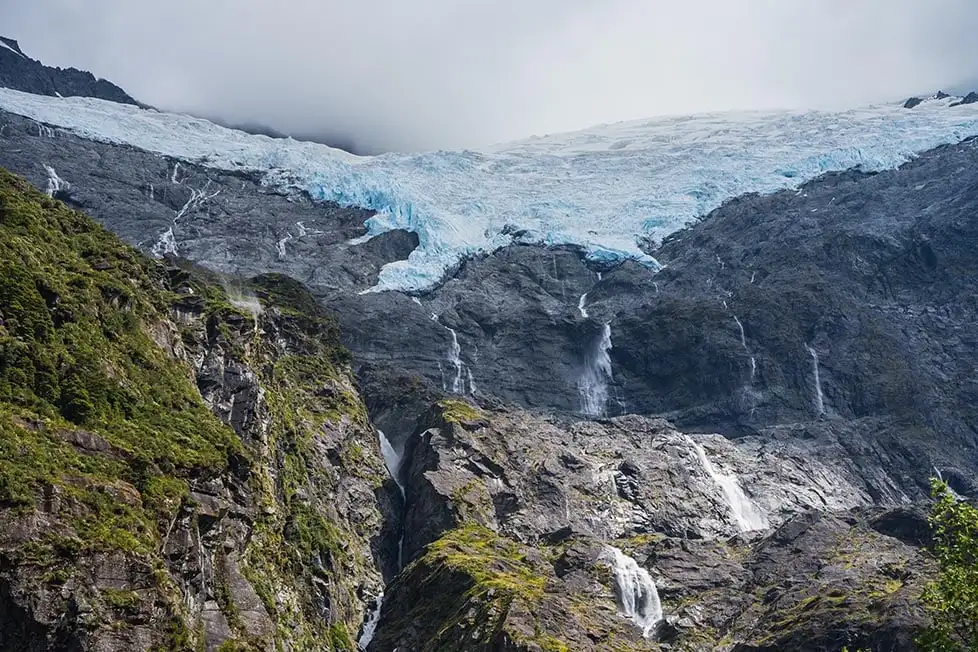 Olhando para uma geleira no topo de uma montanha com cachoeiras caindo perto de Queenstown, Nova Zelândia.