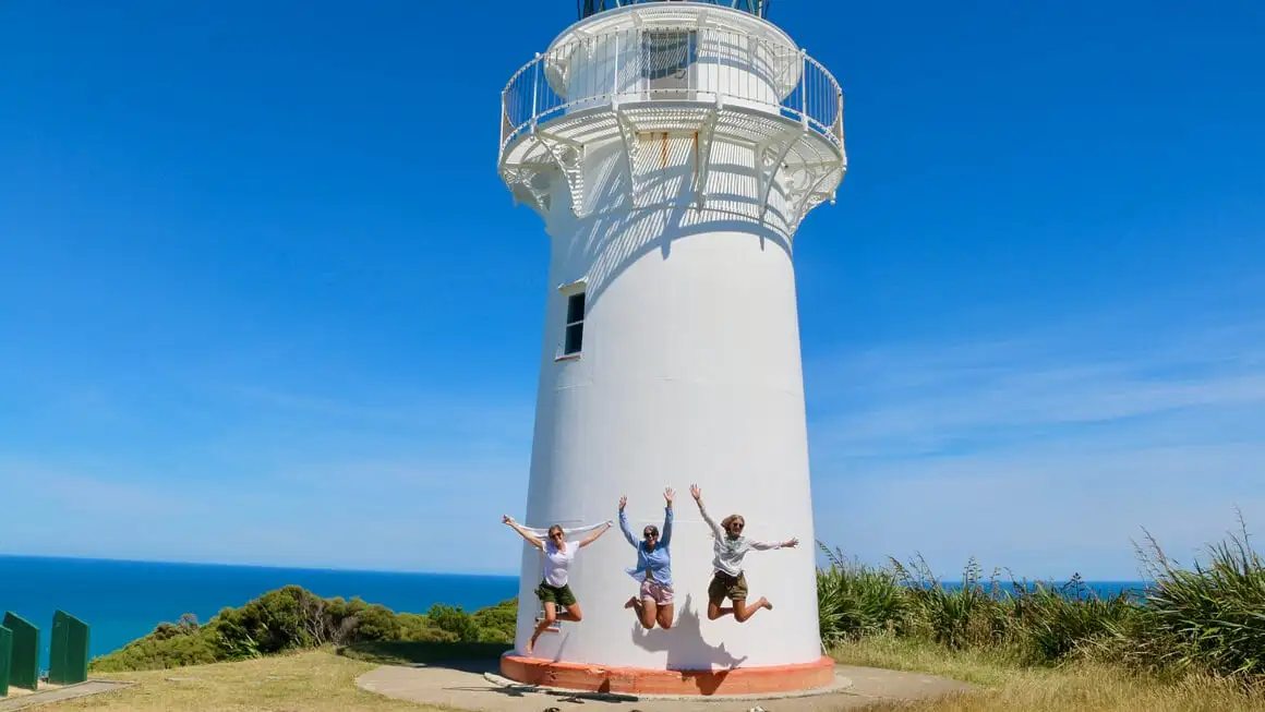 Dani e amigos pulando em frente ao farol de East Cape, Nova Zelândia