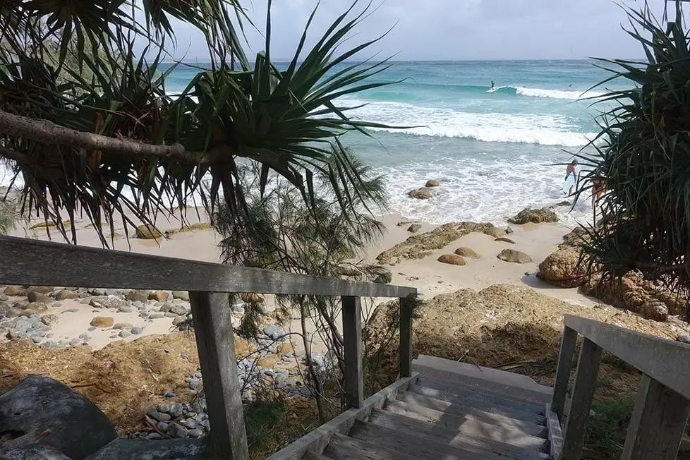 Marches regardant sur la plage avec une personne surfant au loin à Byron Bay, Queensland, Australie