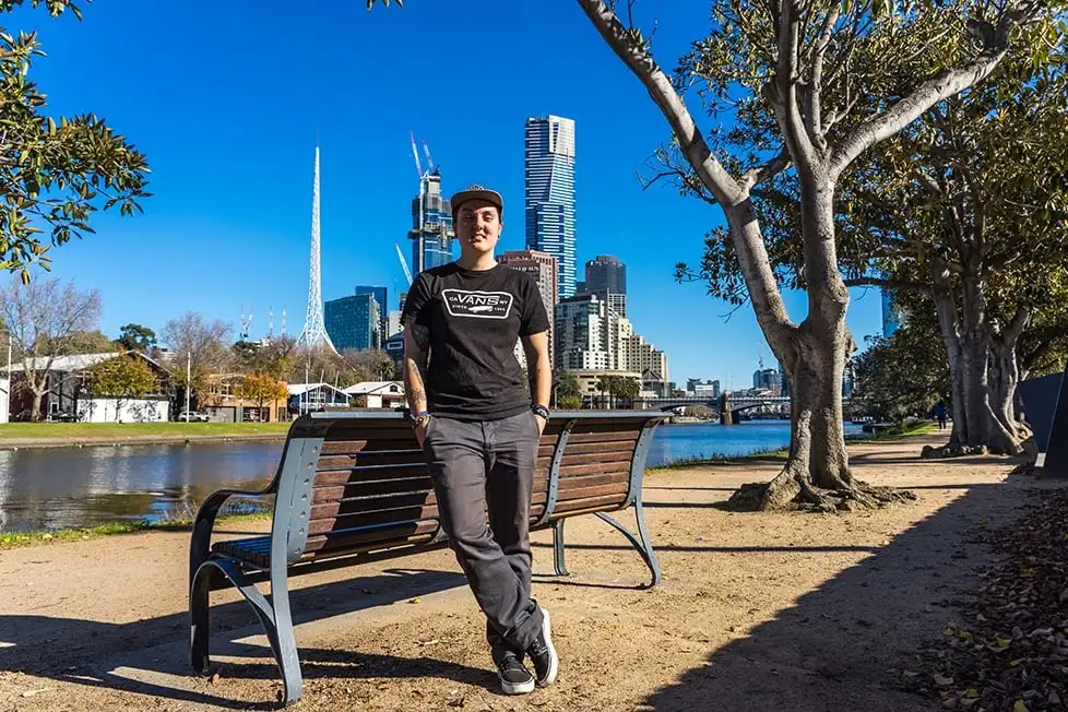 Nic appuyé contre un banc avec l'horizon de Melbourne derrière lui à Melbourne, en Australie.