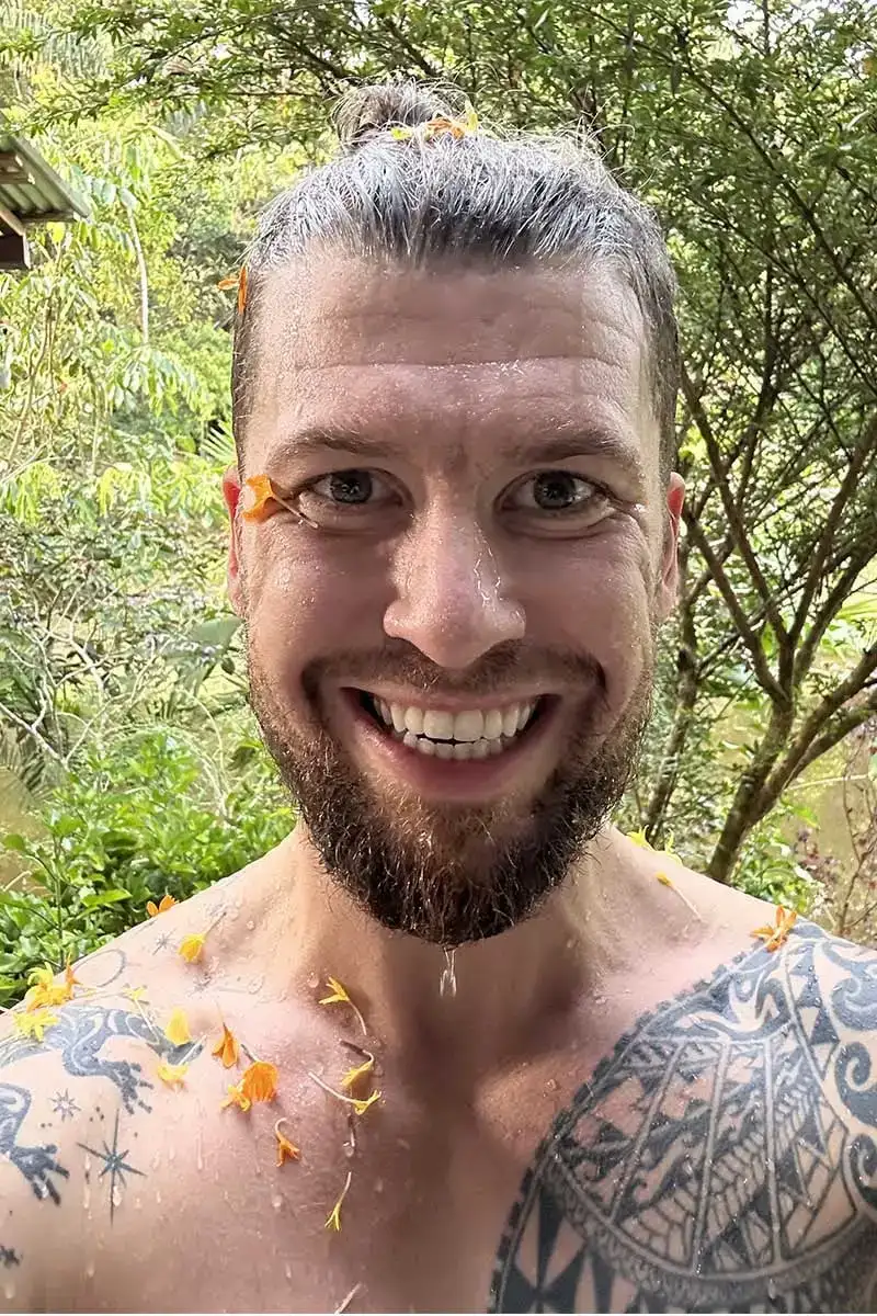 Homme tatoué souriant après un bain de fleurs dans une retraite d'ayahuasca.