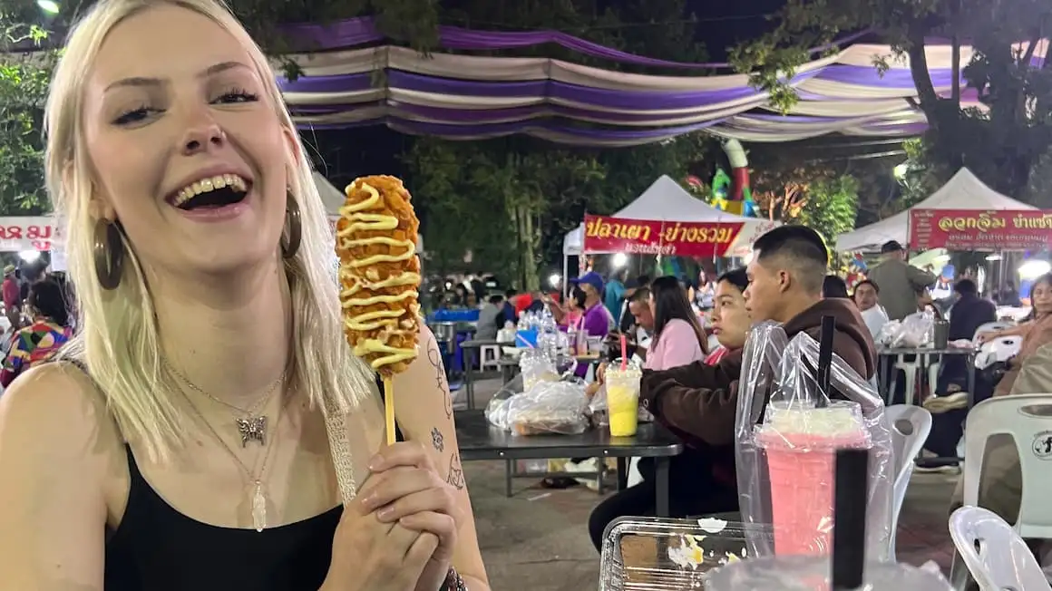 une fille mangeant un chien de maïs sur un marché en Thaïlande