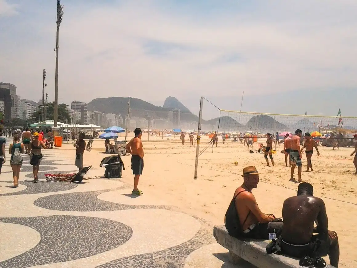 Des gens marchant, assis et jouant au volley-ball par une journée ensoleillée sur la plage de Copacabana à Rio de Janeiro.