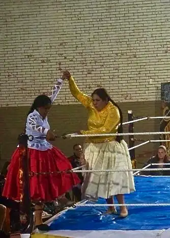 deux lutteurs cholita portant des robes colorées levant les mains ensemble sur le ring