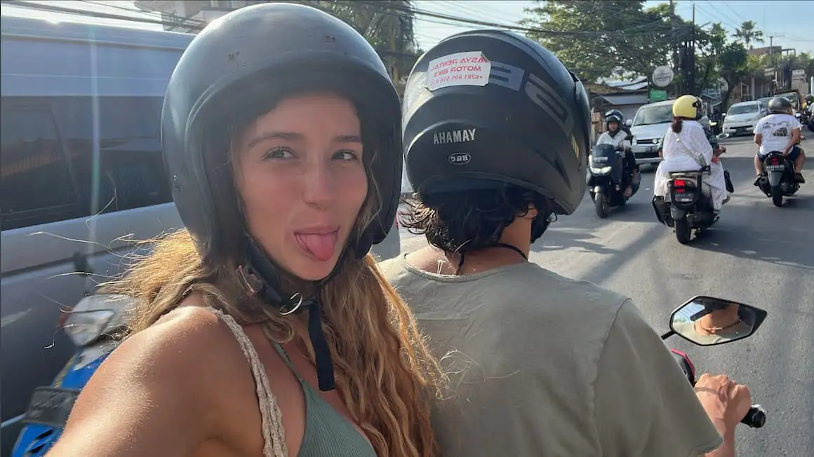 deux filles sur un scooter à Bali, Indonésie tenant un petit chien et avec une planche de surf accrochée sur le côté du scooter