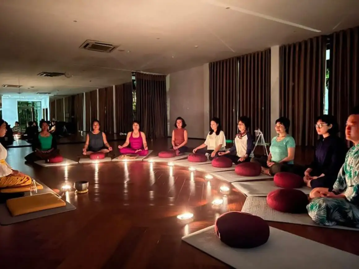 sekelompok orang melakukan yoga dalam posisi duduk di tepi pantai saat matahari terbenam