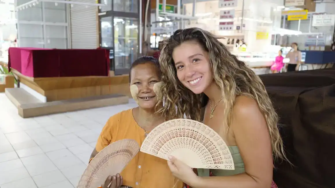 Amanda sorrindo ao lado de um morador em Yangon, Mianmar, segurando um leque