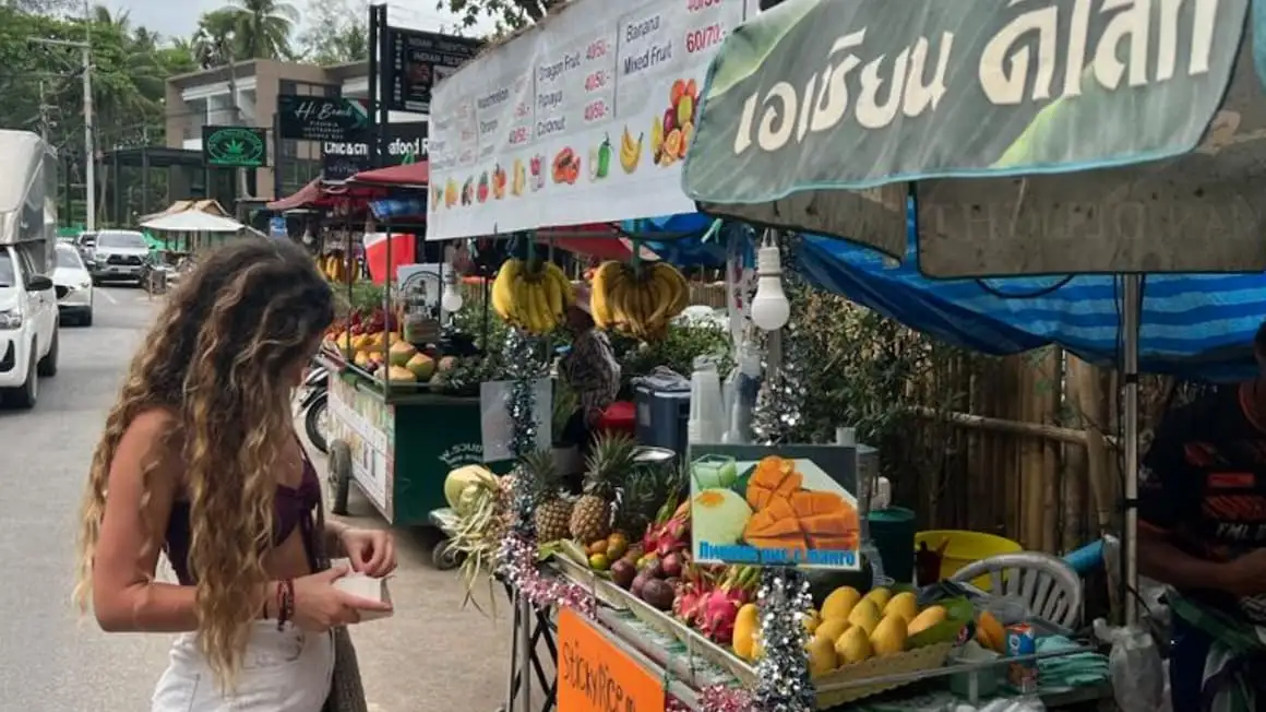 फुकेत, थाईलैंड में एक स्थानीय फल की दुकान से फल खरीदती एक लड़की