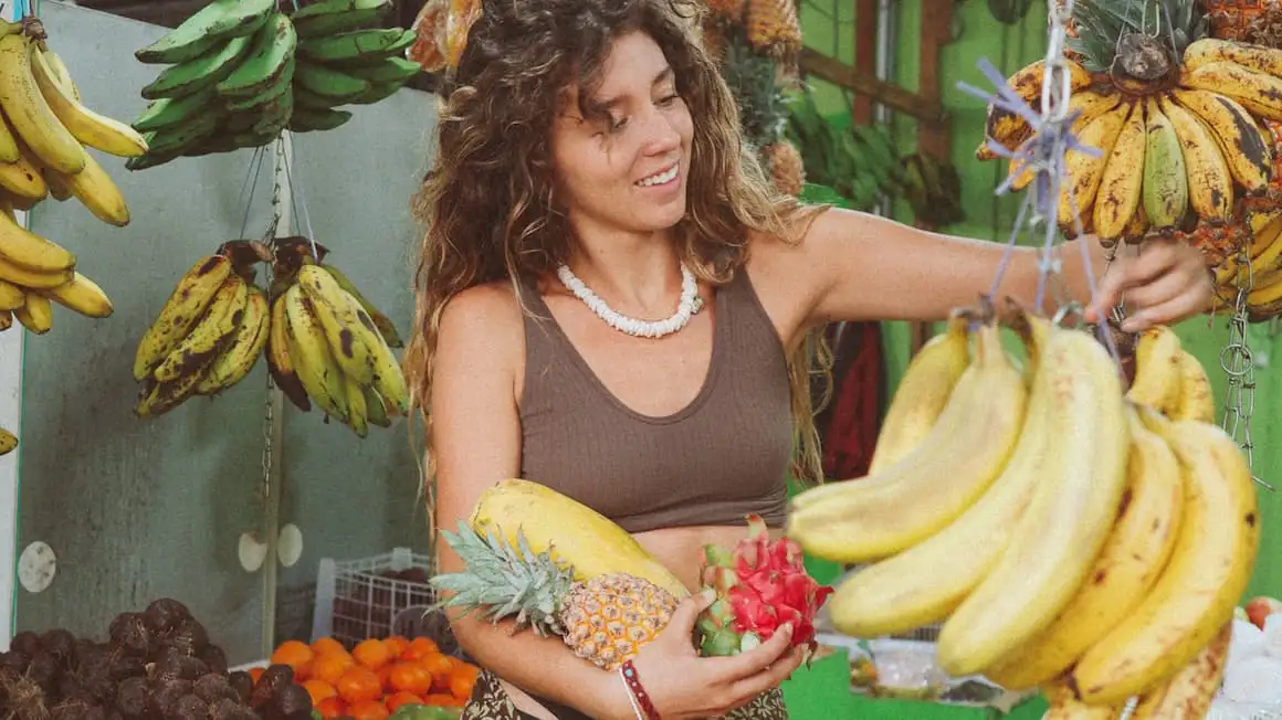 une fille dans un magasin de fruits à Bali, en Indonésie, tenant des fruits du dragon, un ananas et une papaye et cueillant des bananes