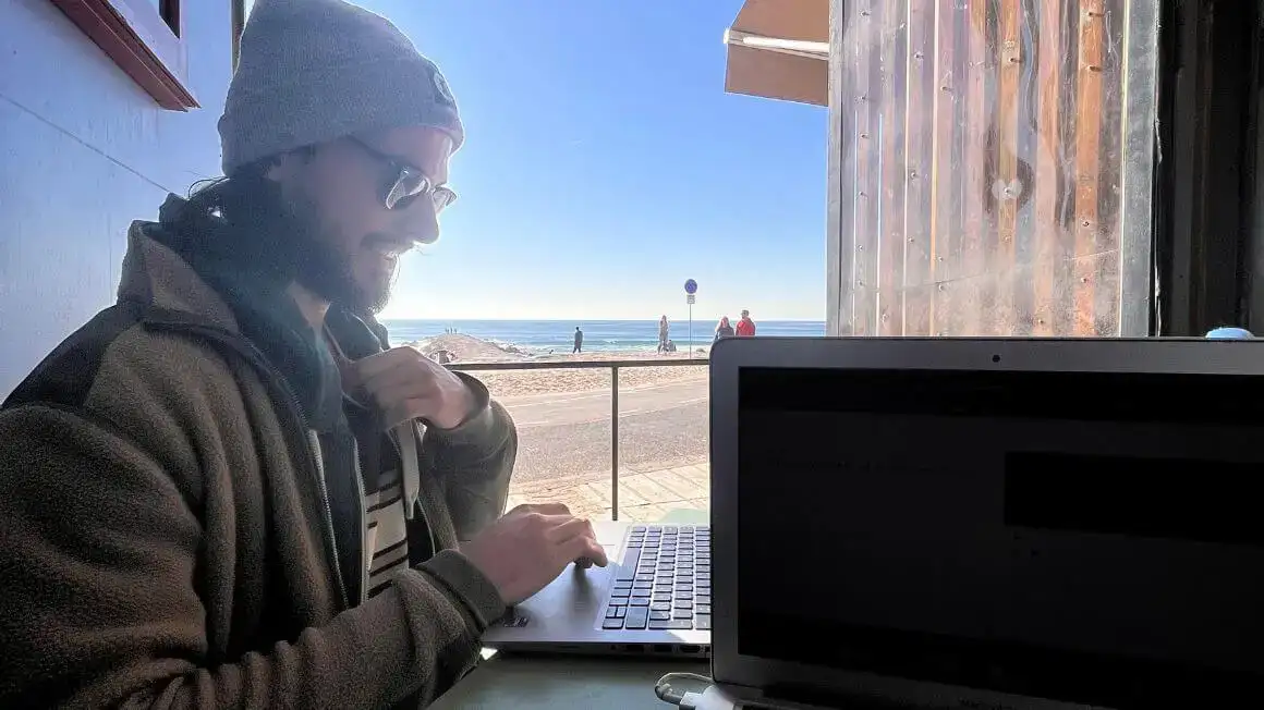 un homme sourit en travaillant à distance sur une plage près de Lisbonne, au Portugal