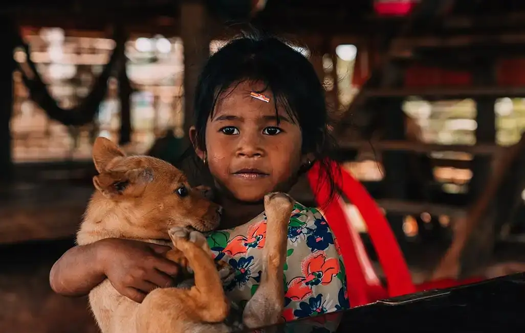 Uma jovem em uma tradicional palafita no Camboja segurando um cachorrinho. Sudeste da Ásia.