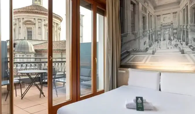 Una cama doble en una habitación de hotel con una puerta abierta que da a una terraza con vistas a una basílica en el B&B Hotel Milano Sant