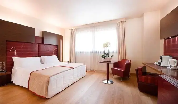 Una cama tamaño king en una espaciosa habitación de hotel con escritorio y mesa pequeña con flores, todo decorado en madera y detalles en rojo en Art Hotel Navigli, un hotel en Milán, Italia