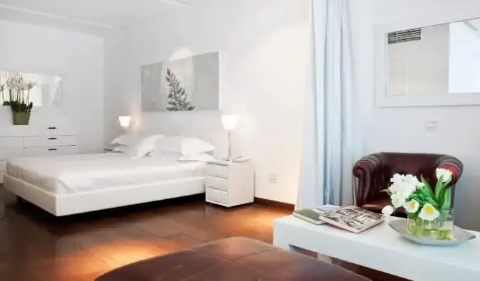 Una cama tamaño king, mesa de café, sillón de cuero y jarrones de flores en una suite de Magna Pars L